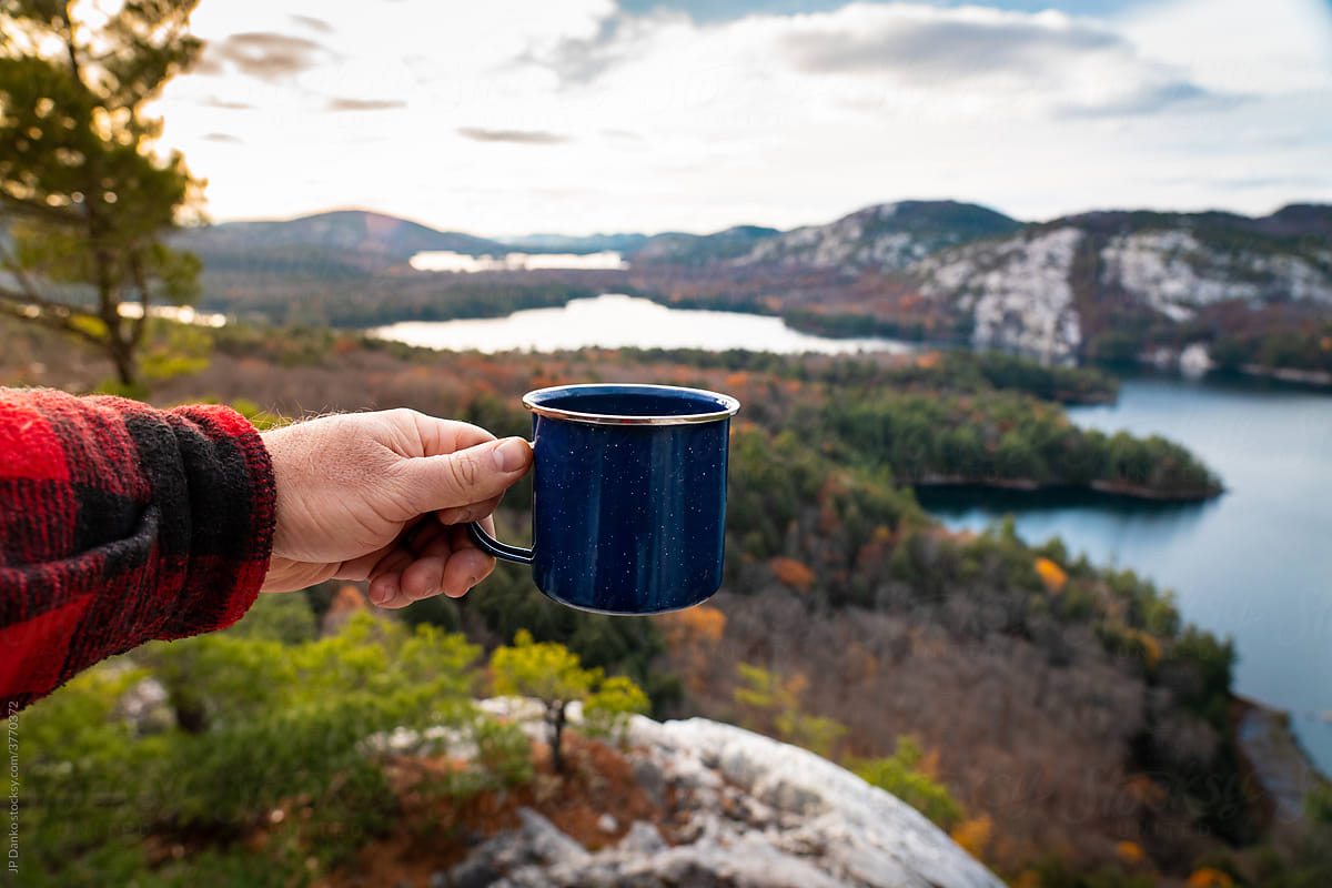 Man Holding Tin Coffee Mug at Mountain Outlook with Forest