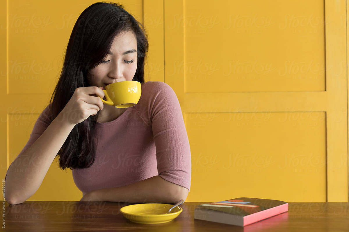 Asian Woman Drinking Coffee With Yellow Background By Stocksy