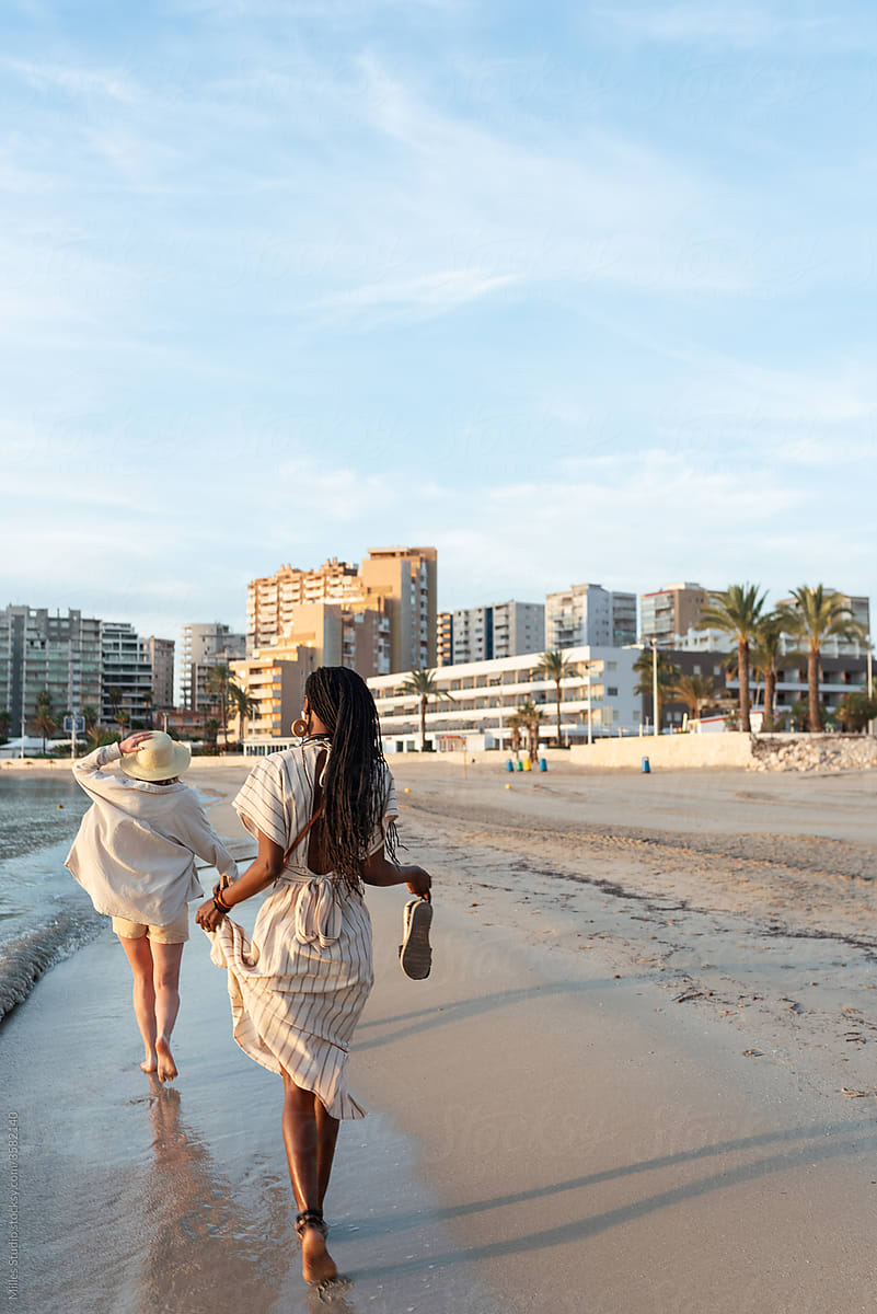 Anonymous diverse girlfriends walking near sea on resort