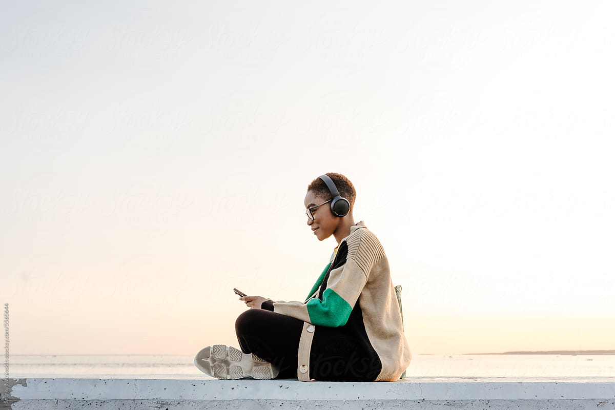 Woman in headphones browsing smartphone at sunset