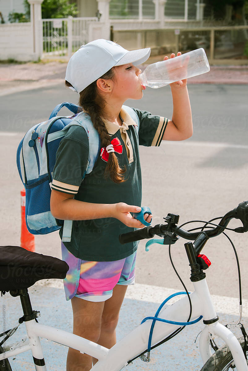 A schoolgirl drinks water from a plastic bottle on a hot day