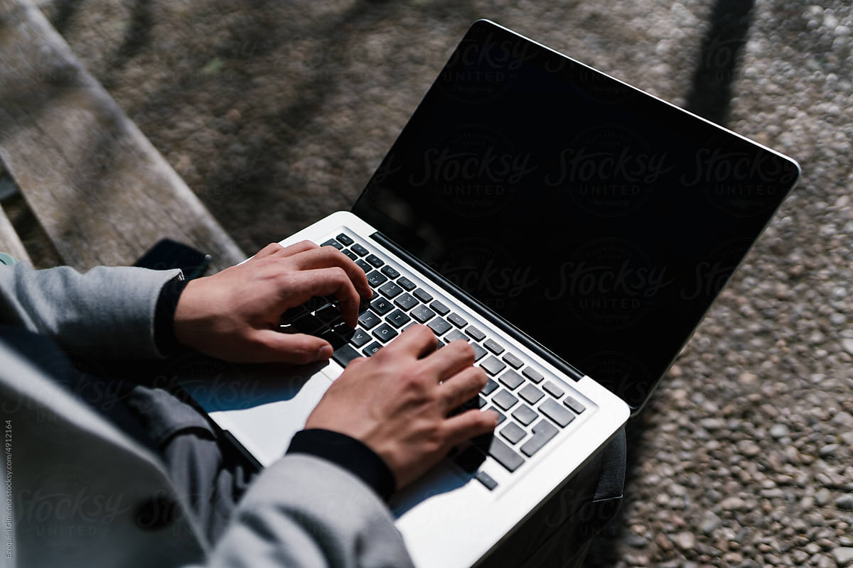 Crop man working online on laptop on bench