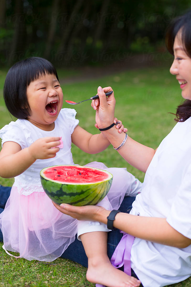 Happy kid eating watermelon with her mother outdoor