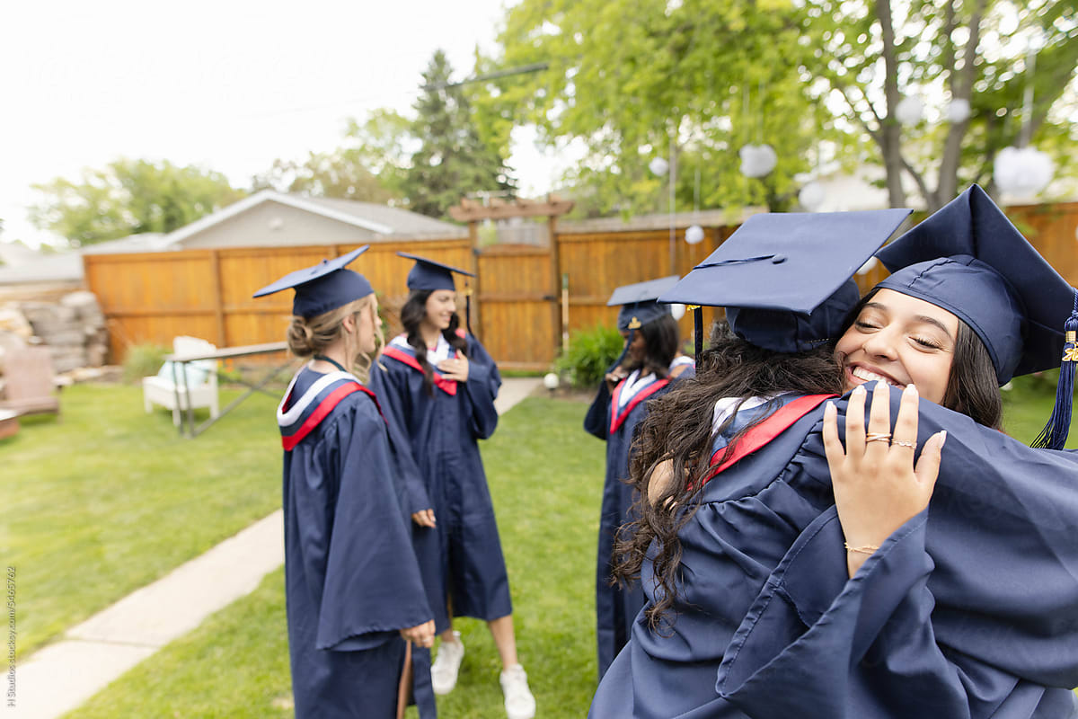 Happy teenage girl graduates in cap and gown hugging in backyard