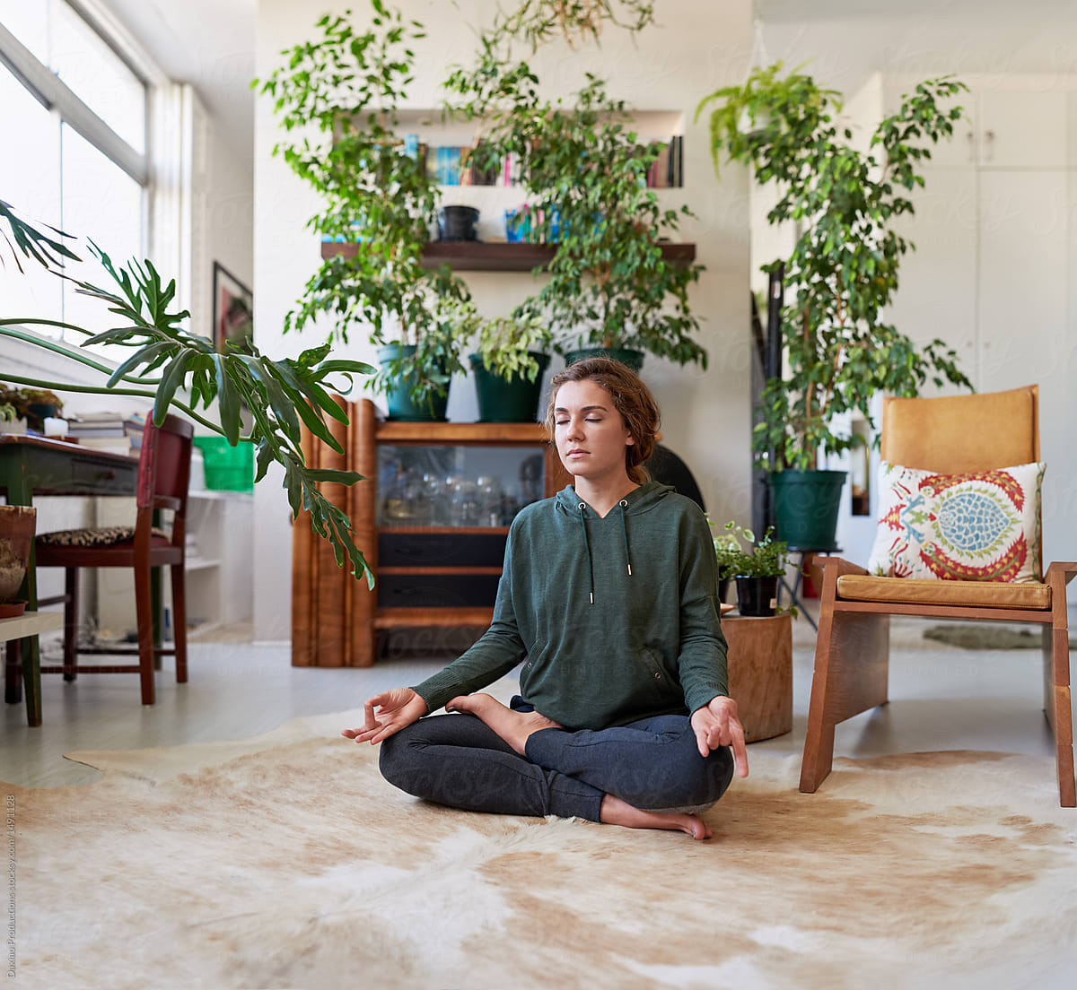 Woman meditating in plant filled apartment