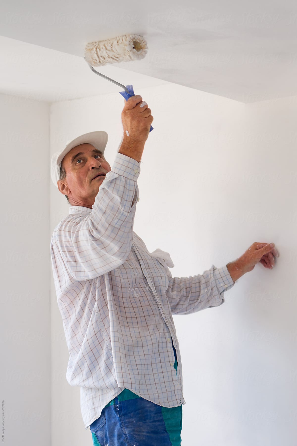 Adult man using a paint roller to paint the indoor walls white