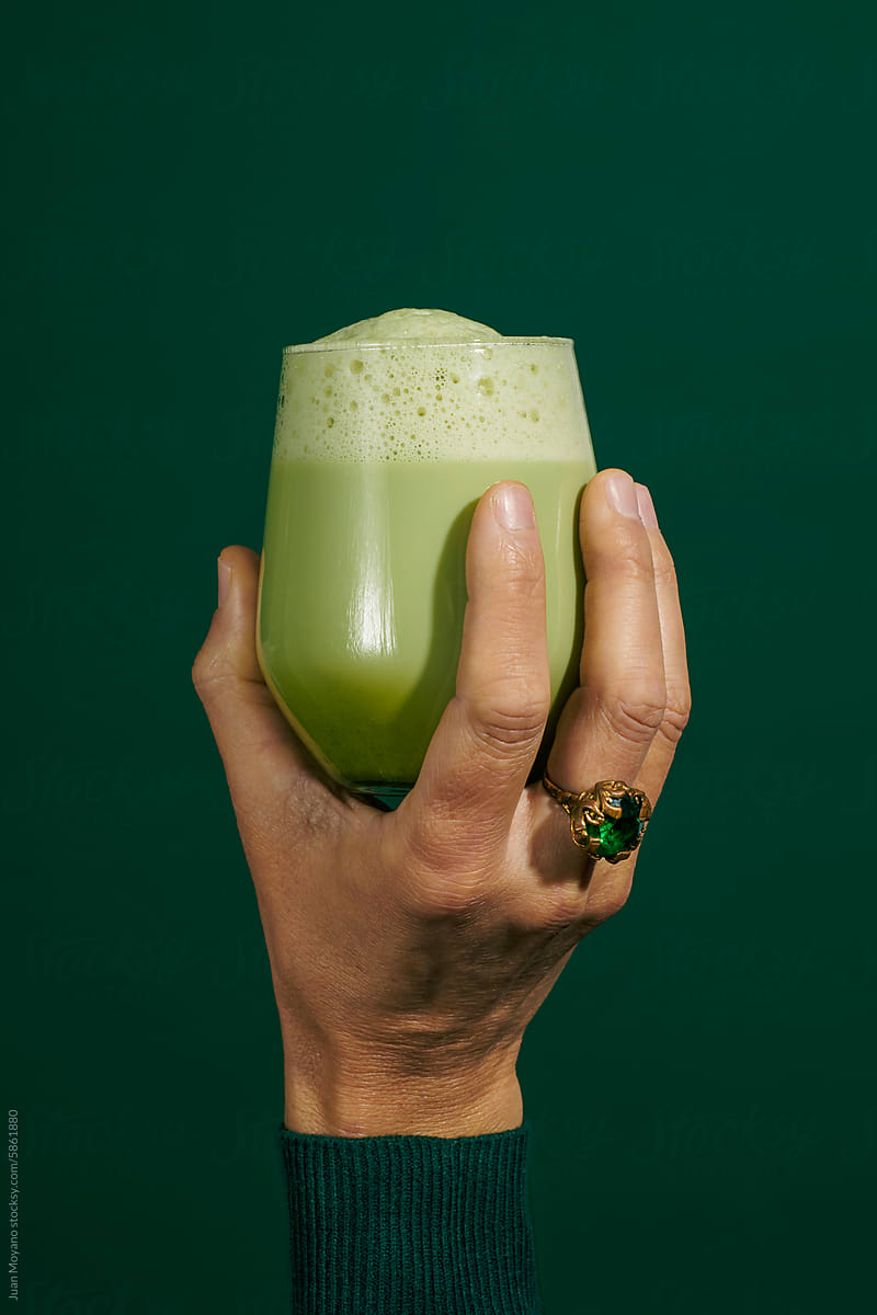 man holding a glass with iced matcha latte