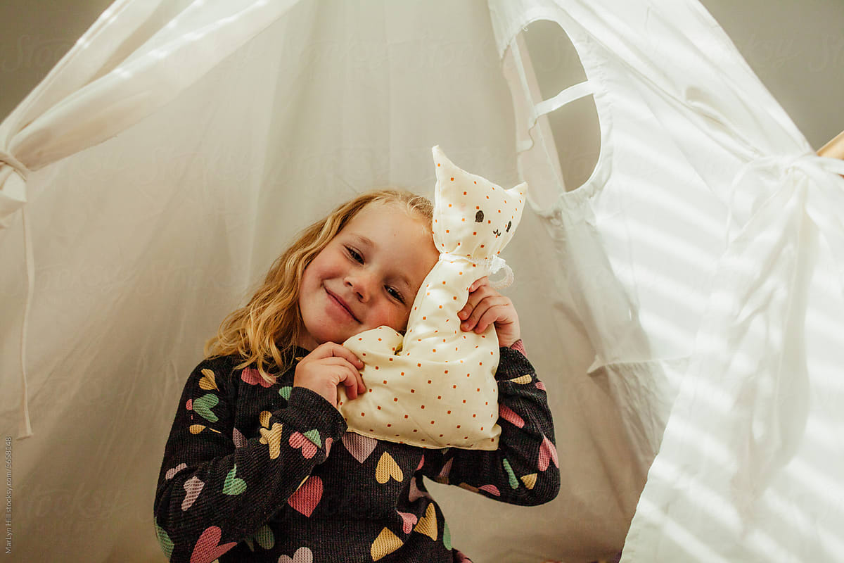 Child holds and leans on cloth cat in tent.