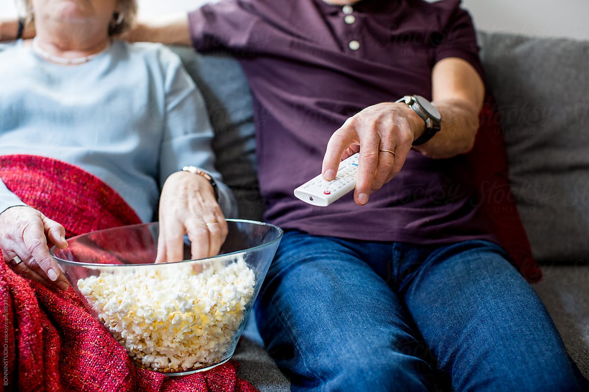 Closeup of an elderly couple watching tv eating popcorn at home.
