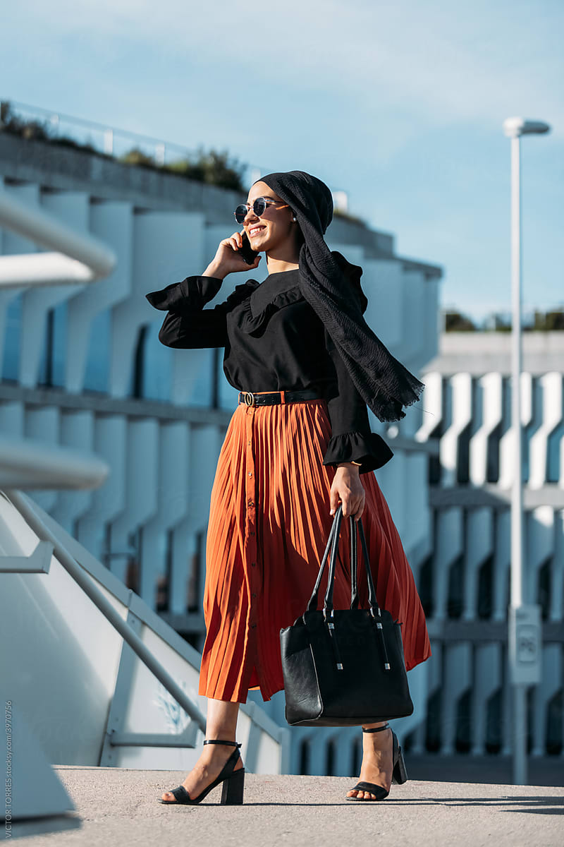 Elegant Muslim woman in stylish outfit speaking on phone on street