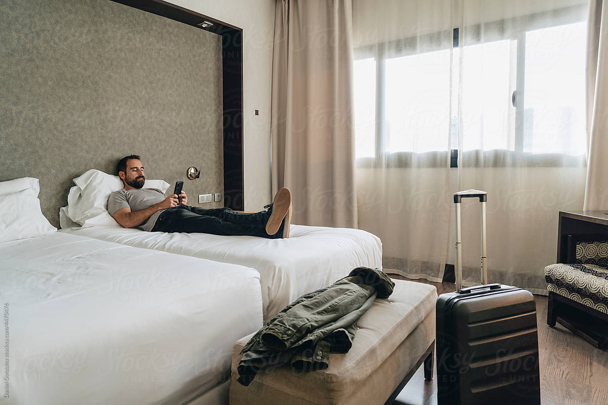 Man resting on bed and browsing smartphone in hotel