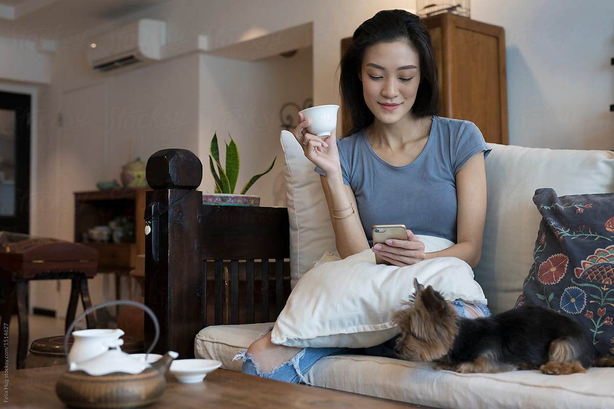 young asian woman on sofa with dog and phone having tea