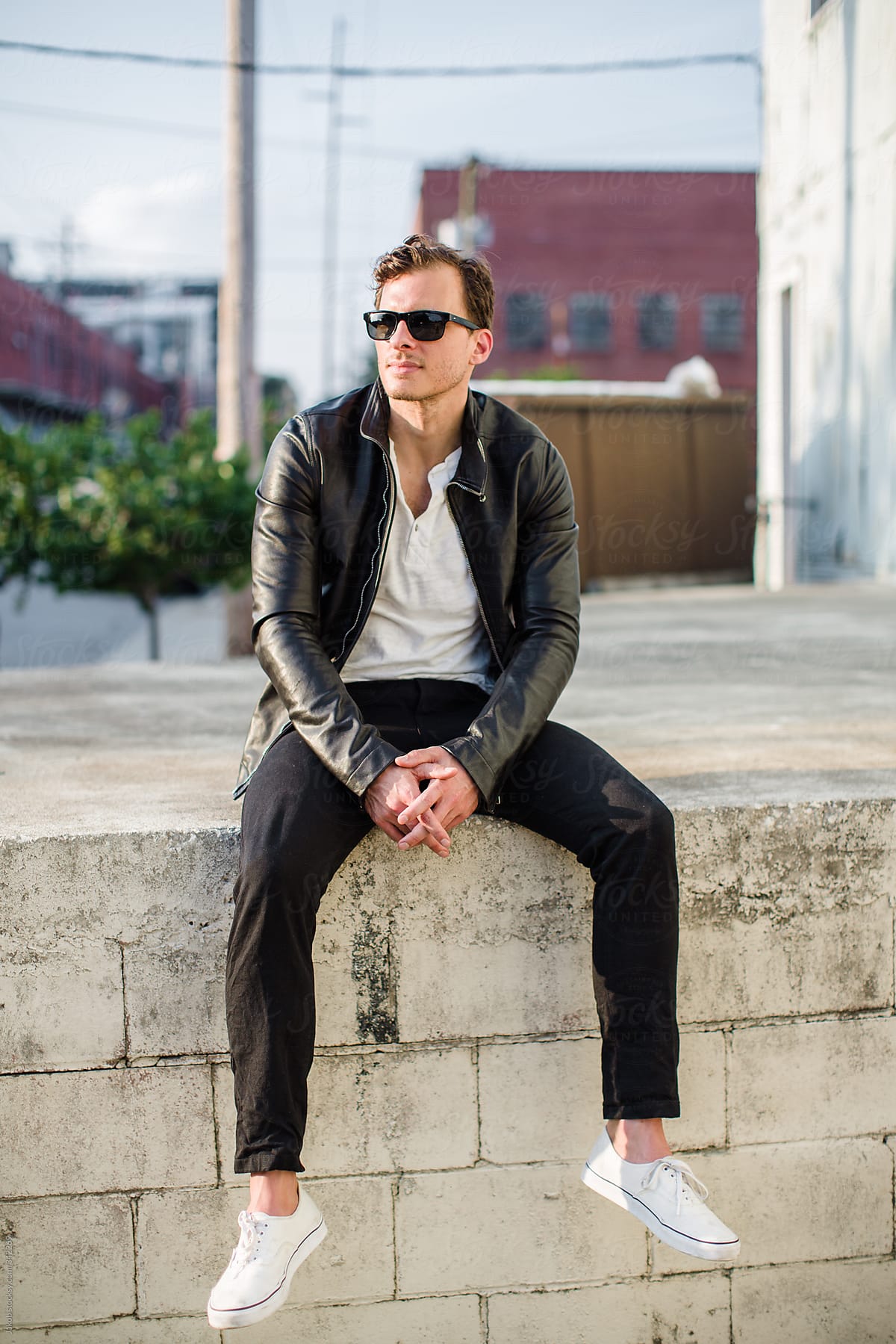 Fashionable man in a leather jacket sitting on a concrete wall