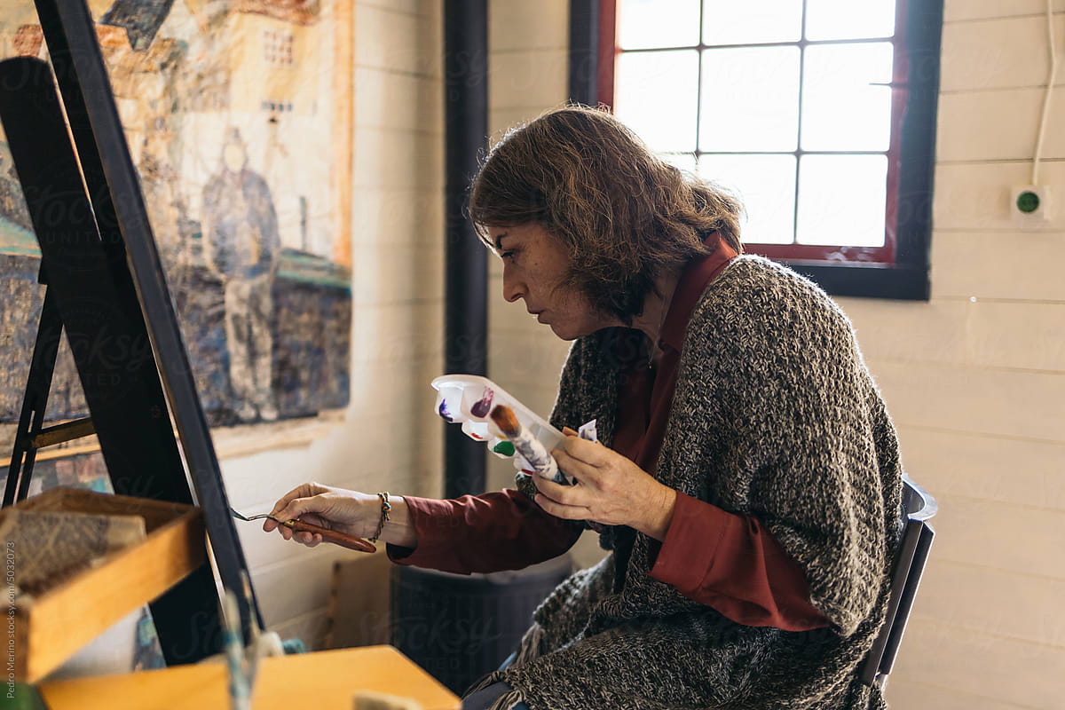 Mature woman artist painting in a small painting workshop