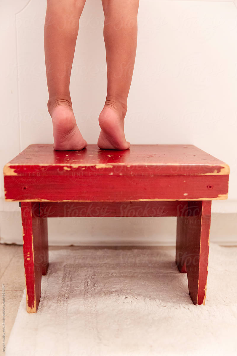 Legs of a child standing on a red step stool