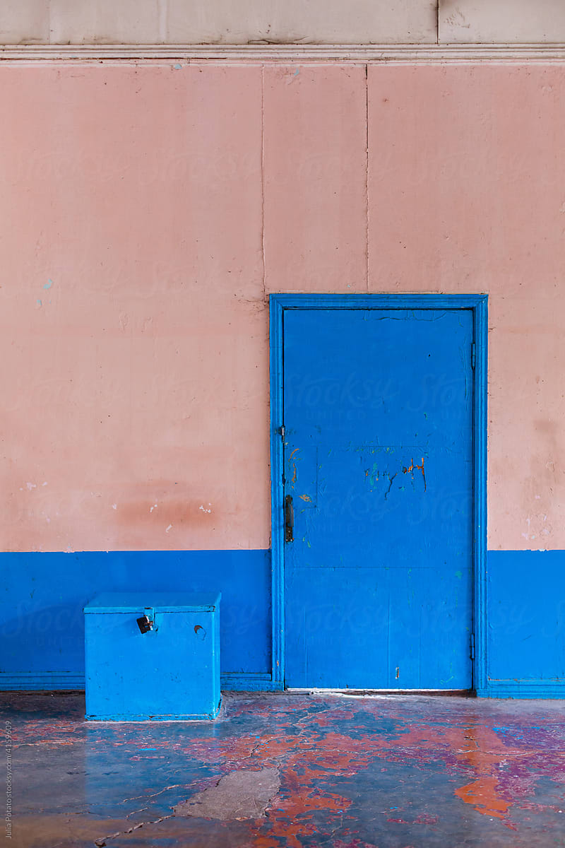 The part of an old coloured wall with blue  door and box near it