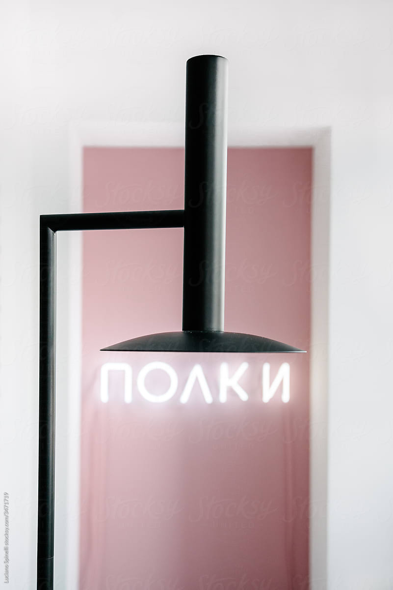 Black lamp in front of a pink wall and a neon light under it