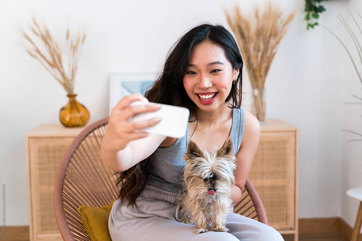 Woman taking a selfie with her little dog at home.