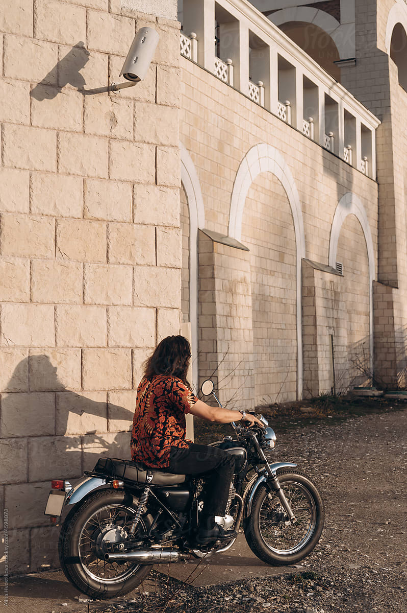 Man taking seat on motorbike near stone wall