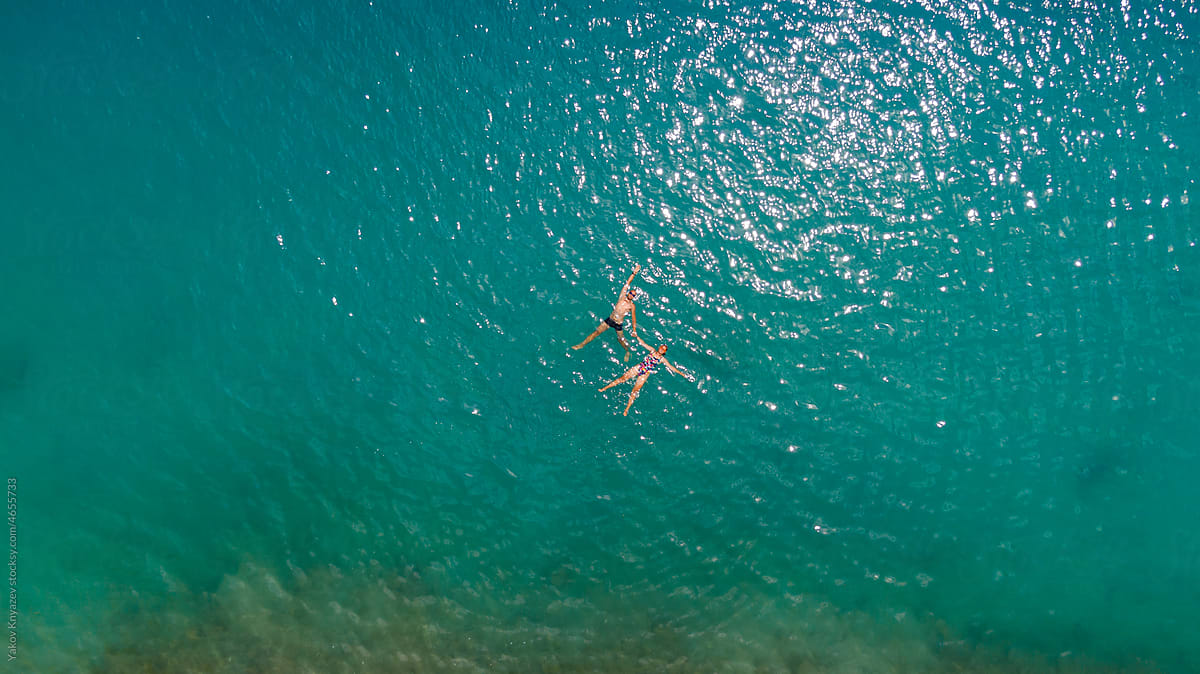 young man and woman in azure water, drone overhead