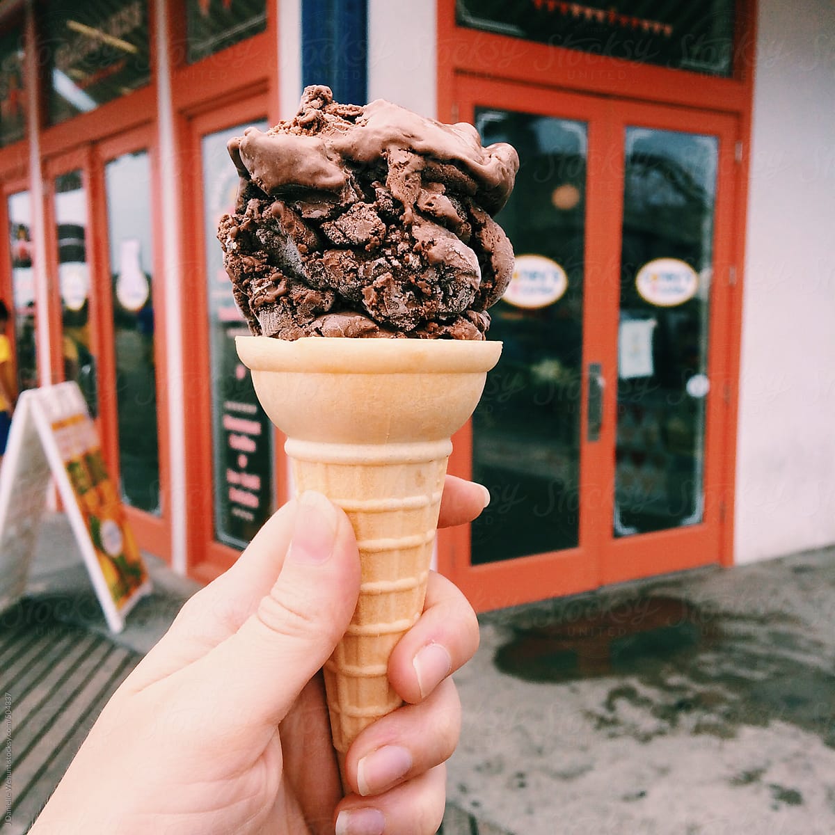 mildly melted chocolate ice cream cone being held by hand in front of store