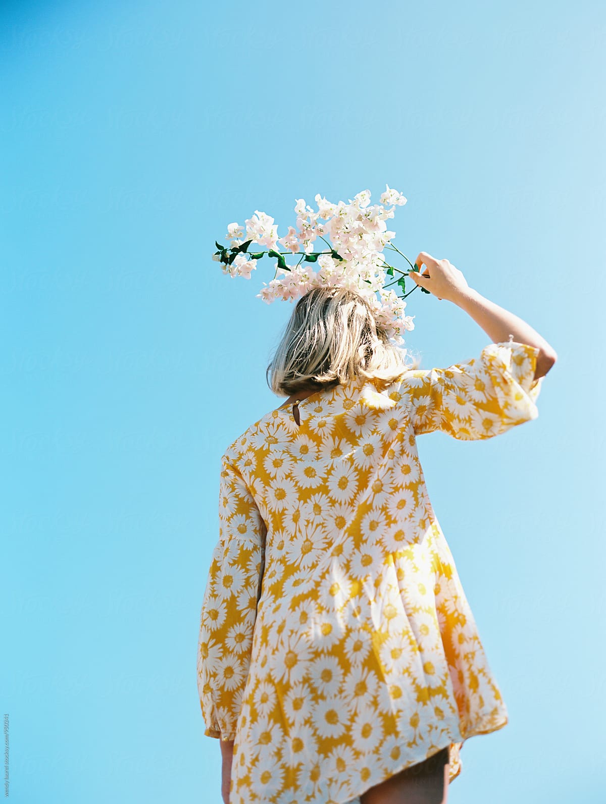 blonde girl with yellow floral dress against blue sky with flowers on her head