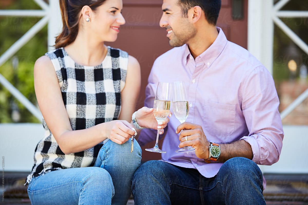 Millennial couple drinking champagne and holding the keys to their first home purchase