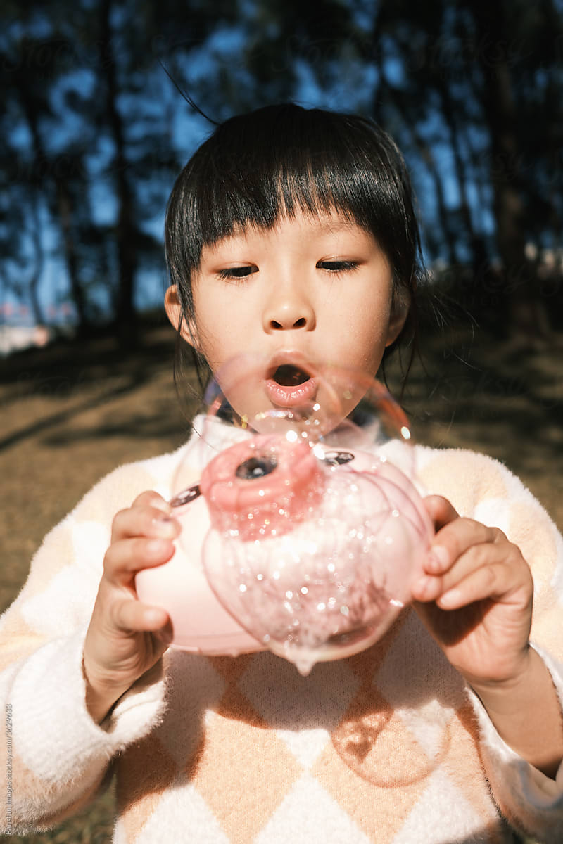 Asian little girl playing bubble machine outdoors