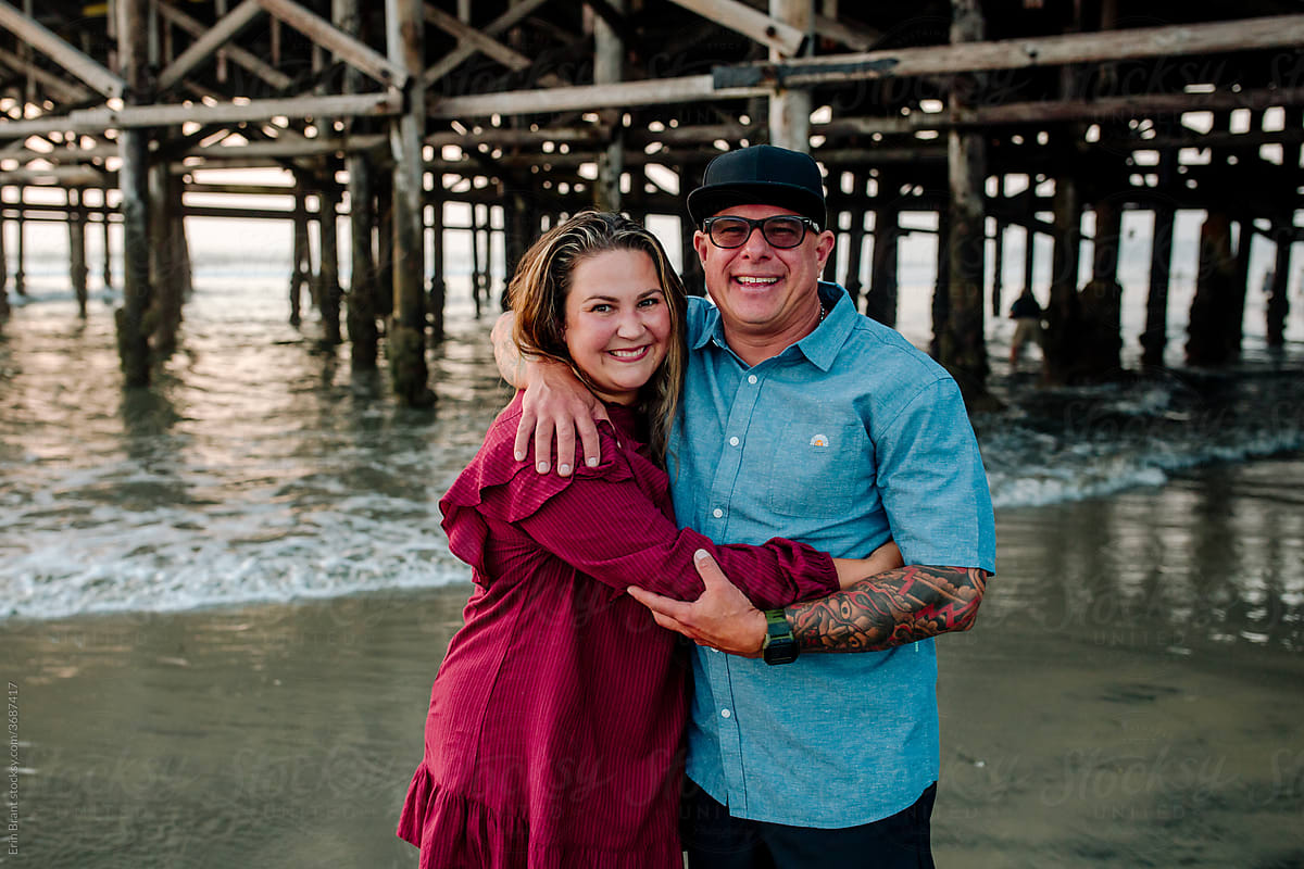 Happy husband and wife share embrace on beach under pier