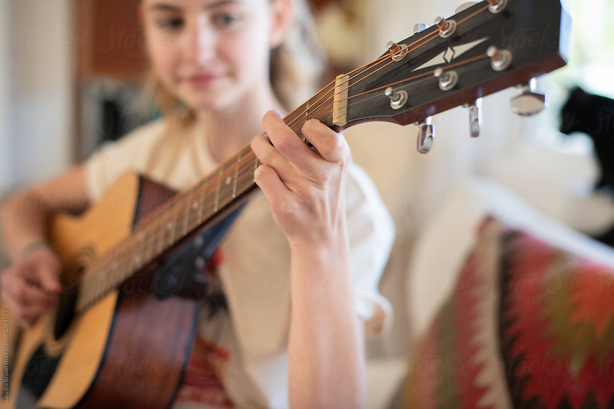 Teenage girl plays acoustic guitar in living room.