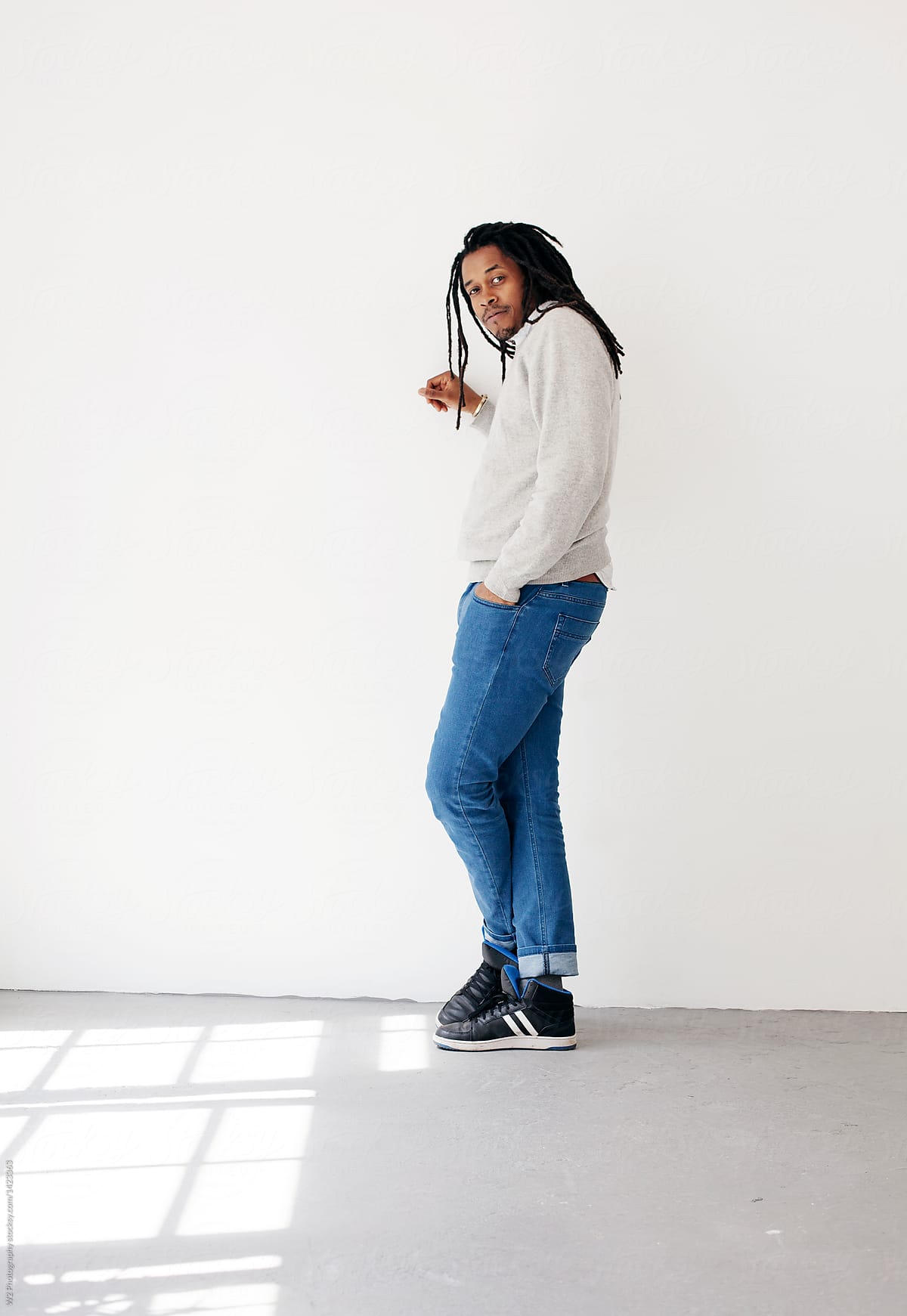 Full body portrait of black man leaning on a white wall.