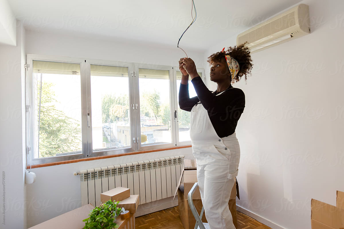 Pregnant woman on ladder fixing electric cable in new home
