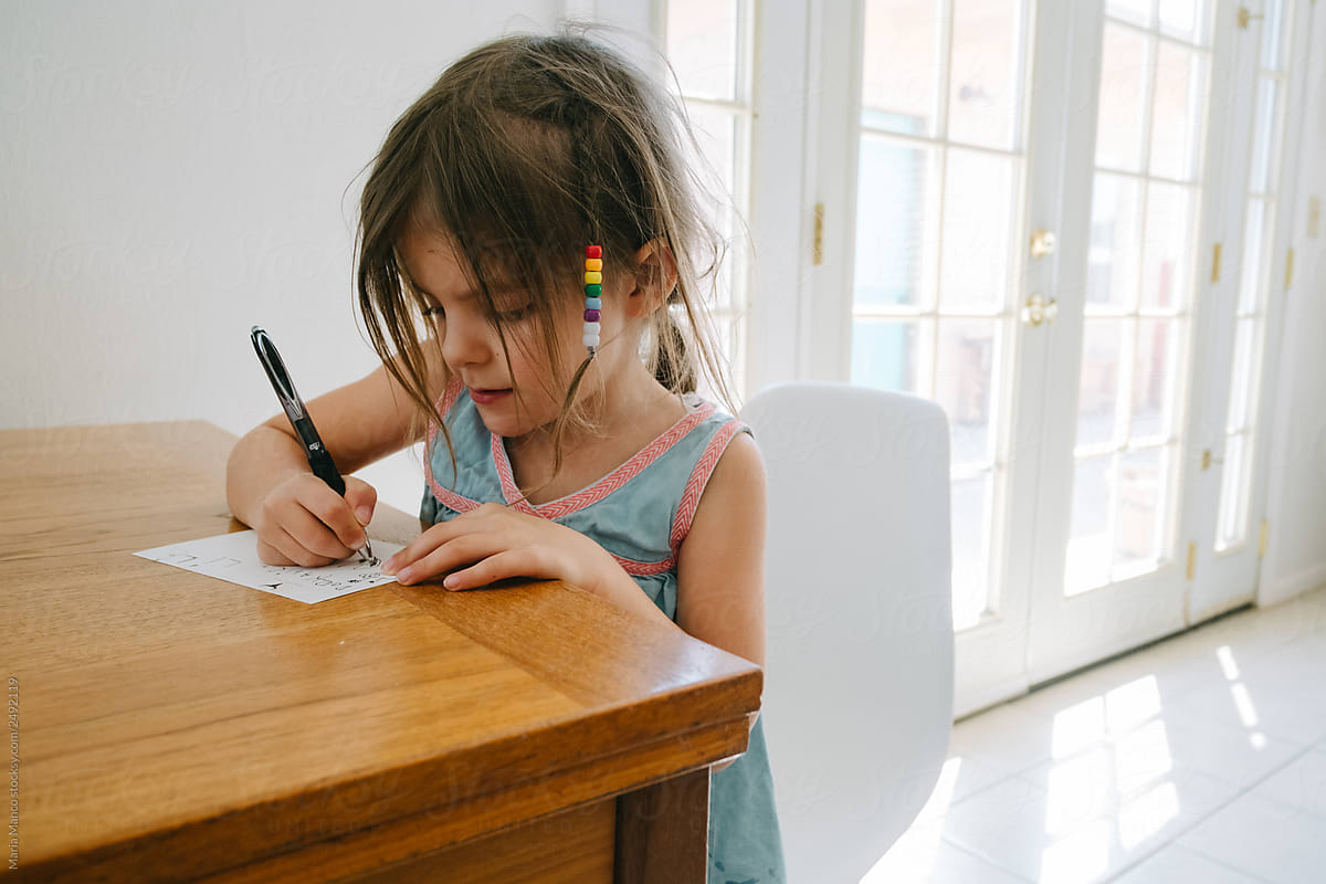 little girl writes a note while sitting at a wood table