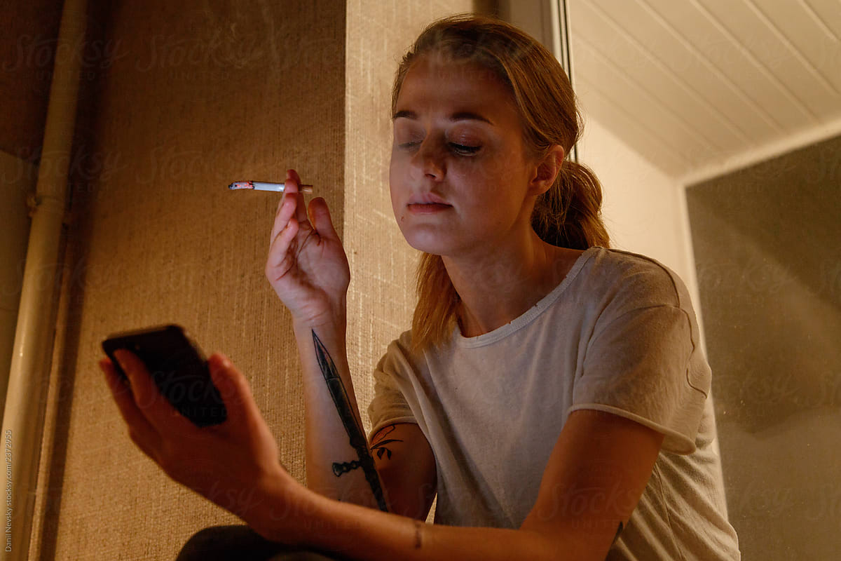 Female with cigarette using smartphone near window