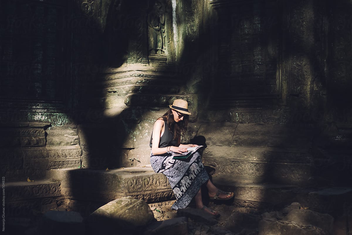 Female Tourist Sitting and Reading a Book in Angkor Wat