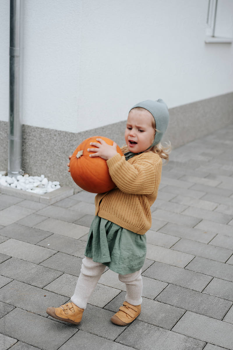 Cute little girl in stylish autumn fashion carrying pumpkin