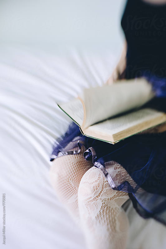 Close up of woman sitting on bed reading vintage book, wearing purple tulle skirt, shot with specialty lens