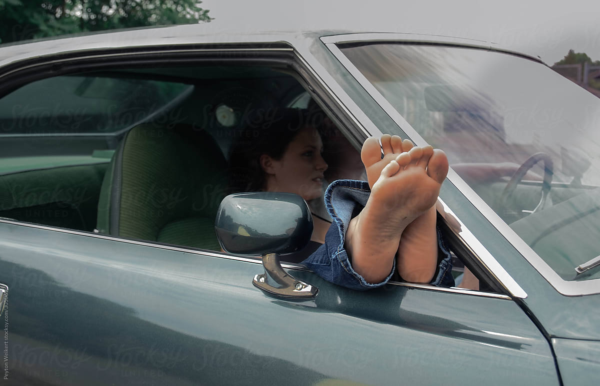 Young Woman In Passenger Seat Of Parked Car With Her Feet Sticking Out