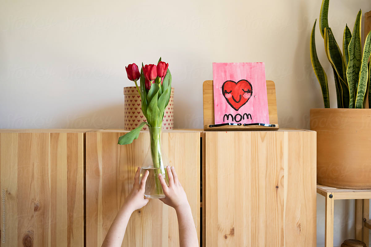 girl´s hand raising a flower vase to a tall cabinet  for mother\'s day
