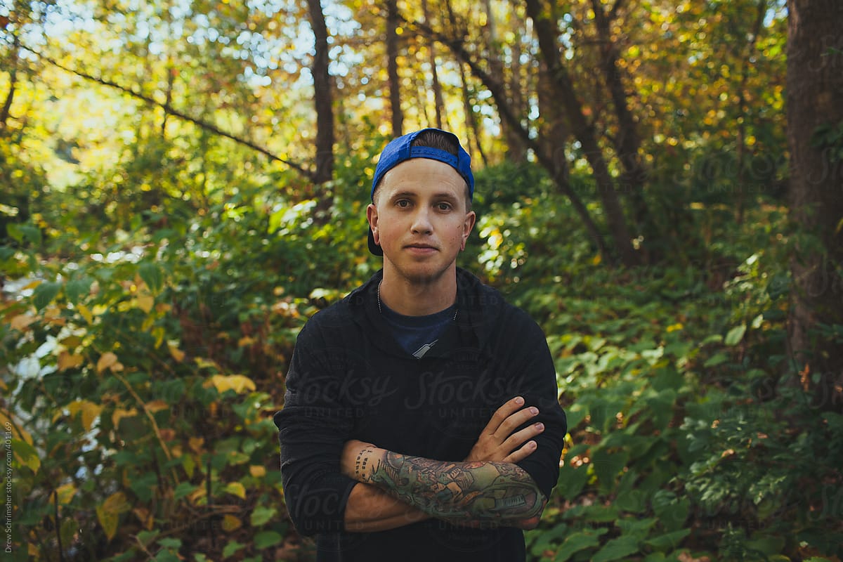 Young male with tattoos and baseball cap poses in forest