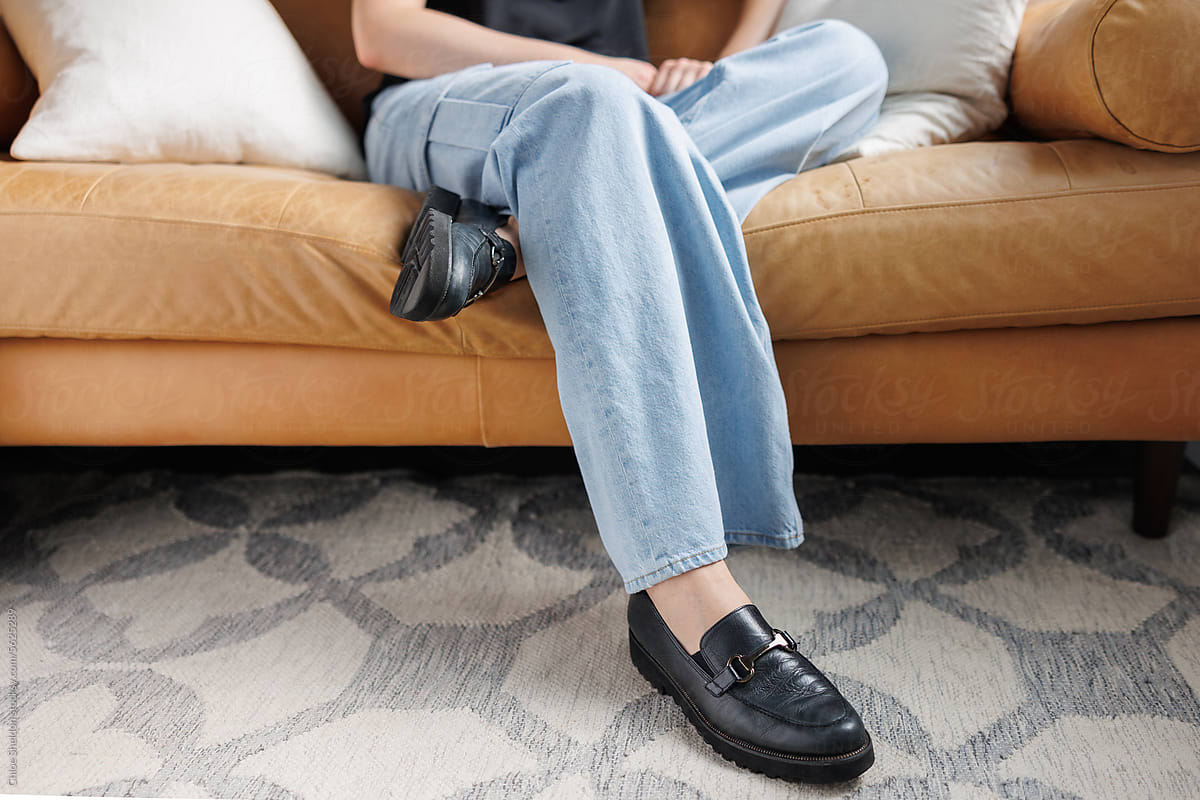 Person in jeans sits on leather couch