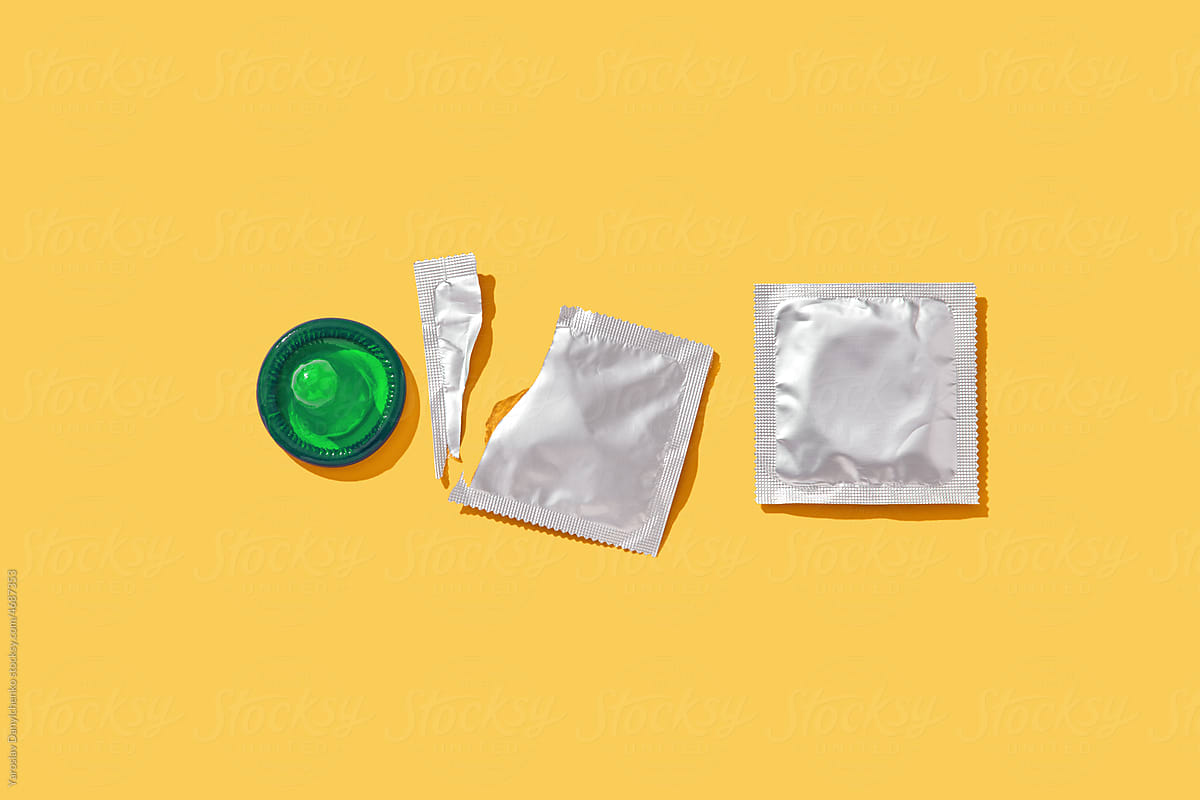 Opened and sealed condoms on yellow background.