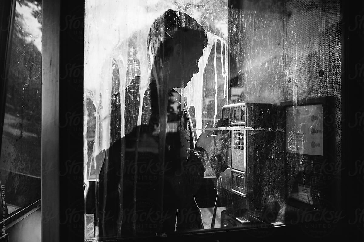 Black and white image of a teenage boy using a phone box that is covered with glue.