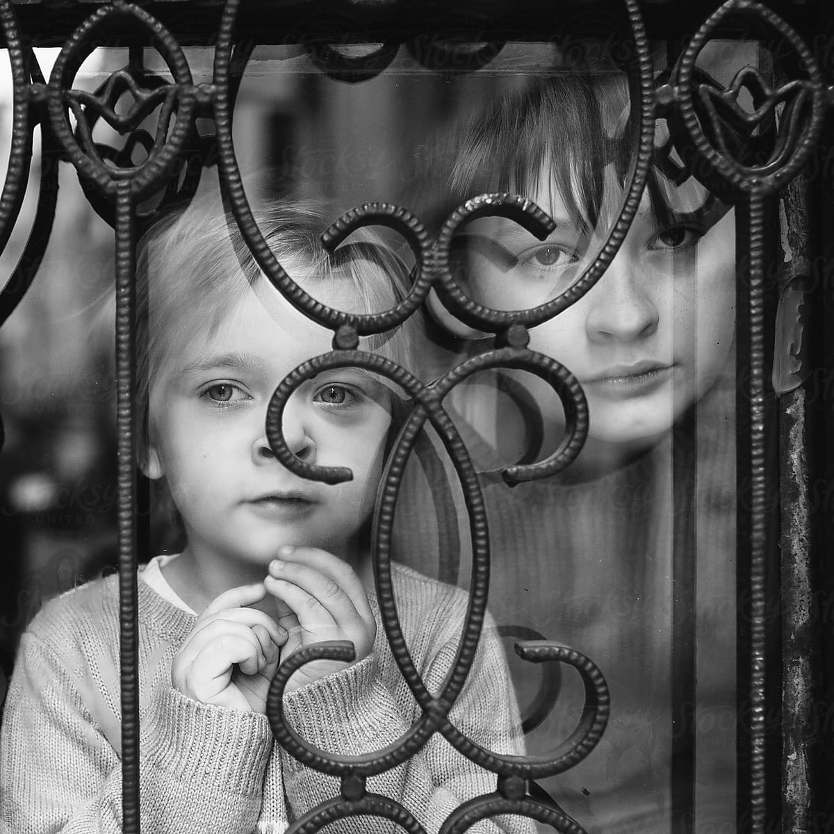 Two children look out of a window with ornate metal bars.