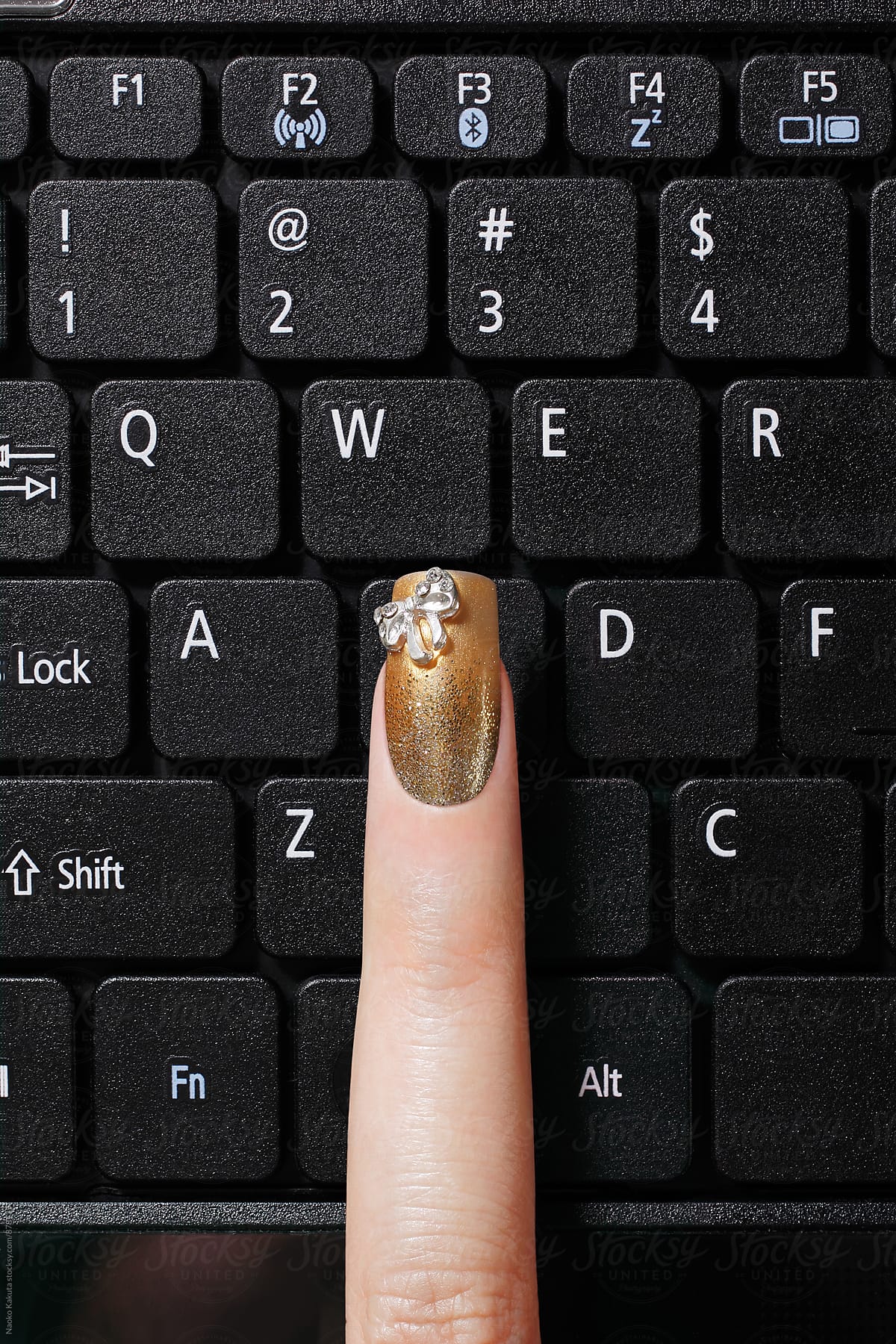 a finger with gold nail polish on black keyboard