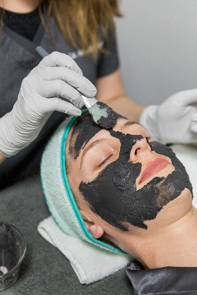 A woman applying black charcoal mask onto woman\'s face