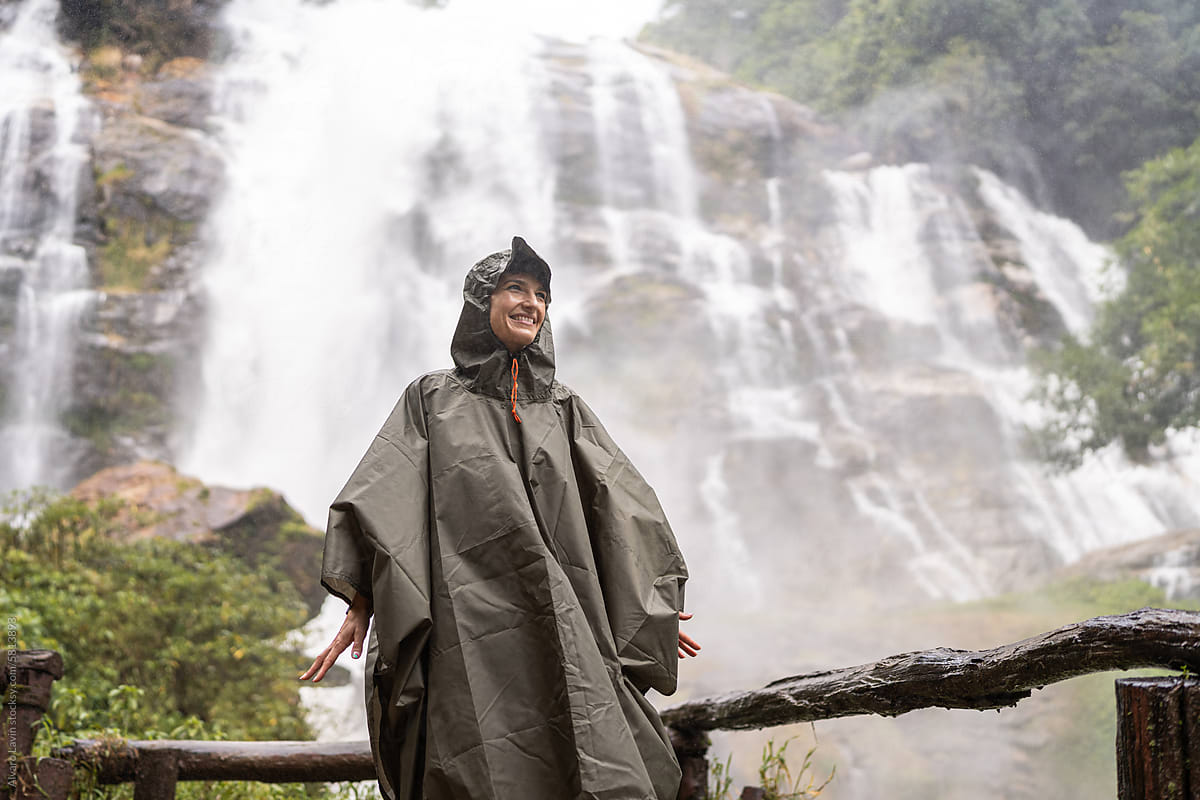 Woman in raincoat near waterfall.