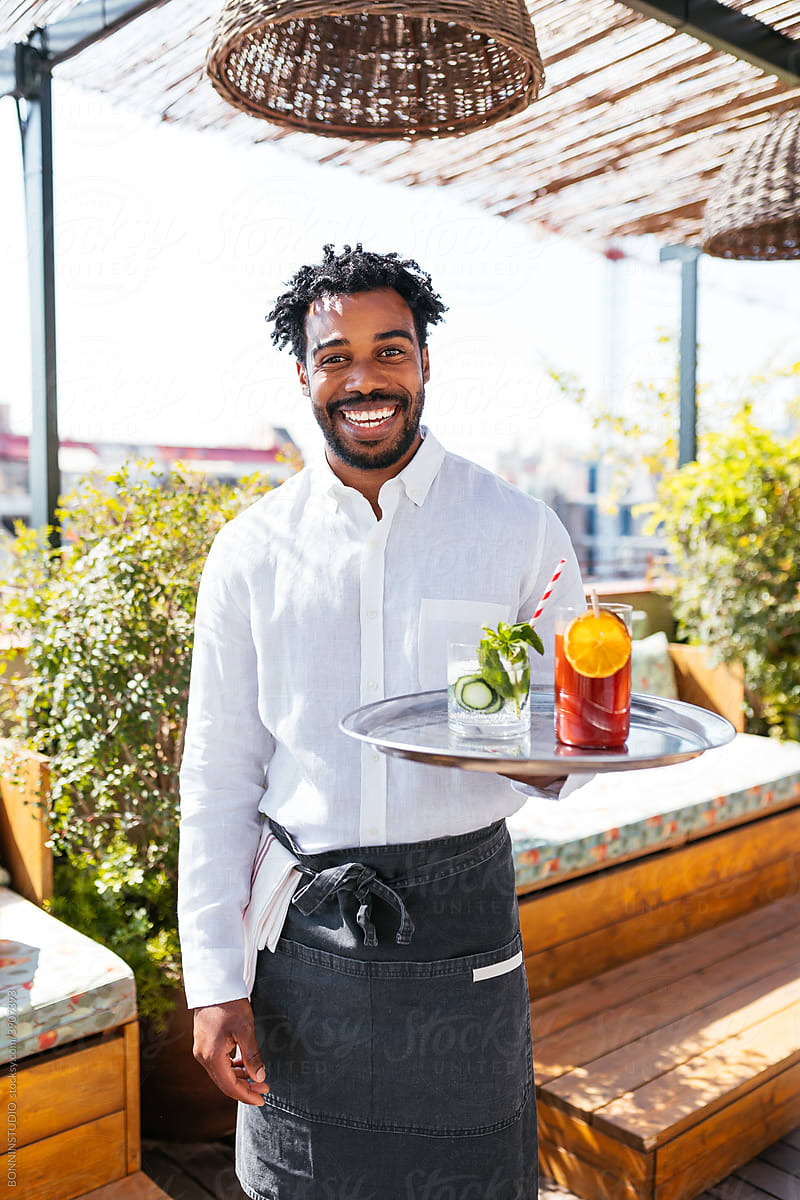 Black waiter with fresh drinks standing on cafe terrace