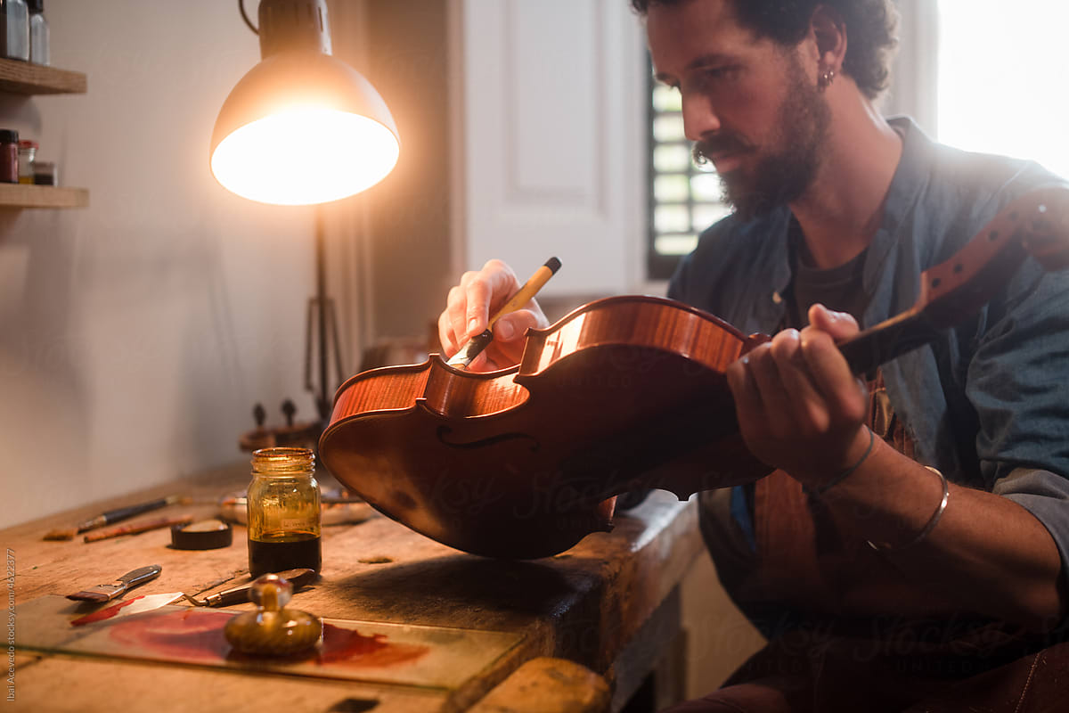Focused craftsman varnishing an old violin