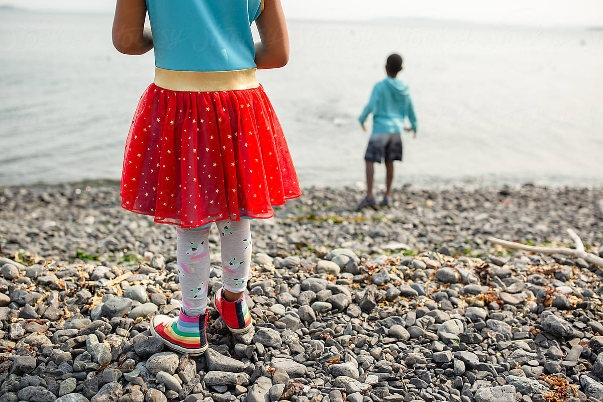 Girl in colorful dress and shoes stands on rocky beach